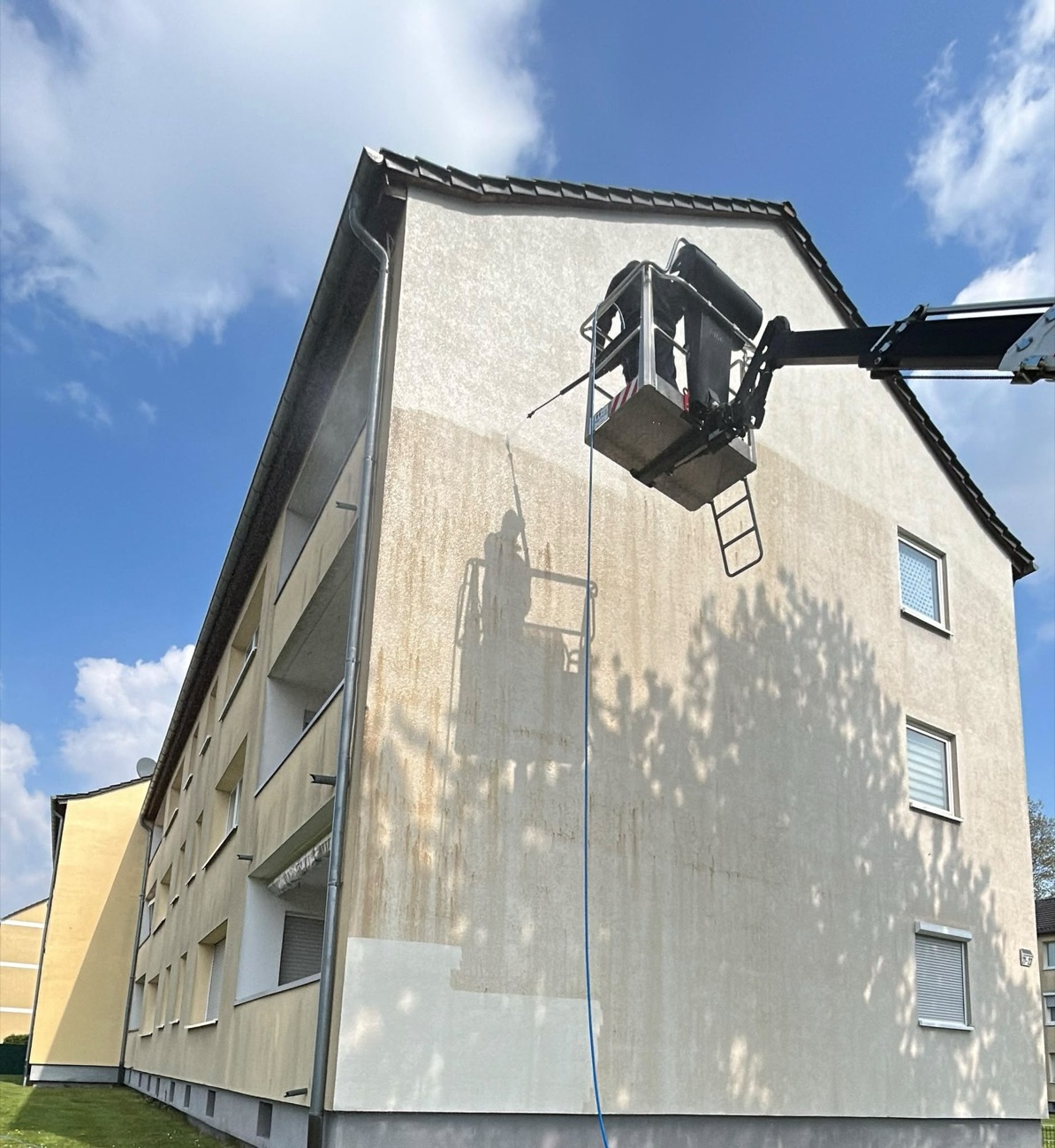 Mehrfamilienhaus während der Fassadenreinigung von der Hebebühne aus, linke Hälfte schon sauber