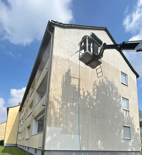 Fassade eines Mehrfamilienhauses, halb gereinigt, mit Hebebühne